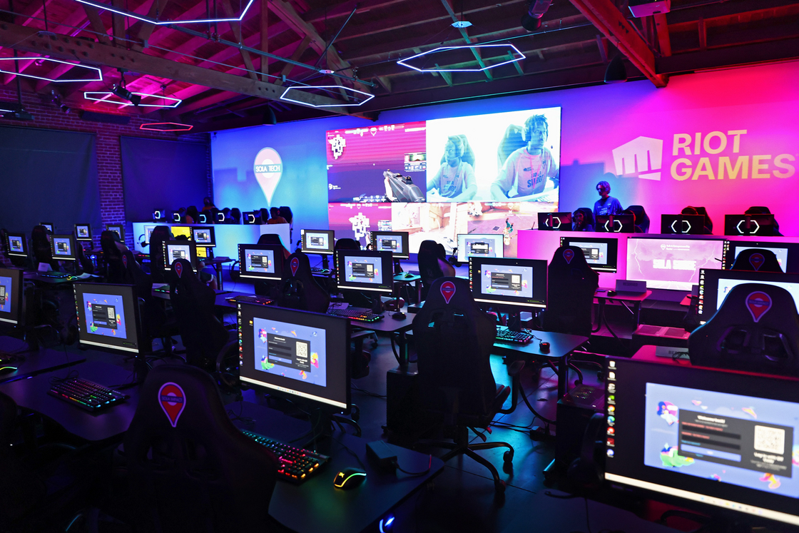 Five esports players sitting in a row at a gaming facility communicating during a match